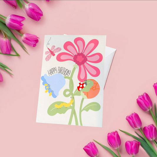 A vibrant spring-themed birthday card featuring three colorful flowers in full bloom with small insects playfully walking over them. The design includes a cheerful handwritten-style 'Happy Birthday' text, adding a fun and whimsical touch. The background is bright and fresh, capturing the joy of nature and celebration. Printed on high-quality white cardstock, this handmade card comes with a matching envelope, perfect for gifting.