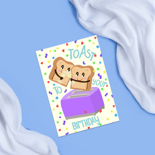 a light beige card with colorful confetti on the background and two pieces of toast , toasting with champagne glasses . the toast is coming out of a purple toaster  and it has the text toast to your birthday around it.