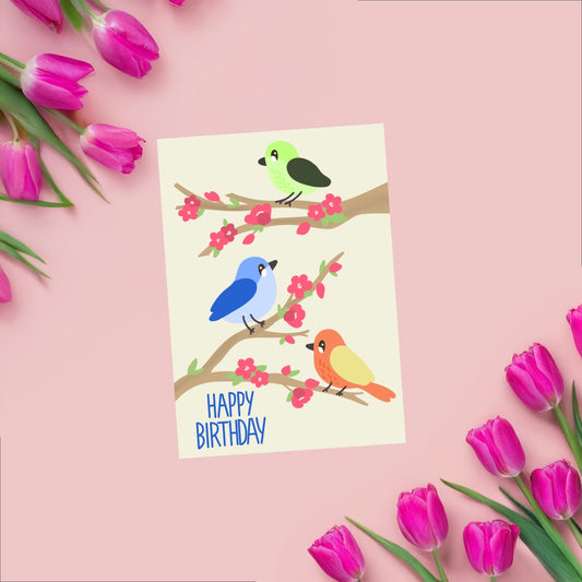 A playful birthday card design featuring three colorful birds perched on tree branches decorated with pink flowers. The soft and cheerful illustration is set on a clean background, making the artwork and colors pop. A whimsical and handmade card perfect for birthdays