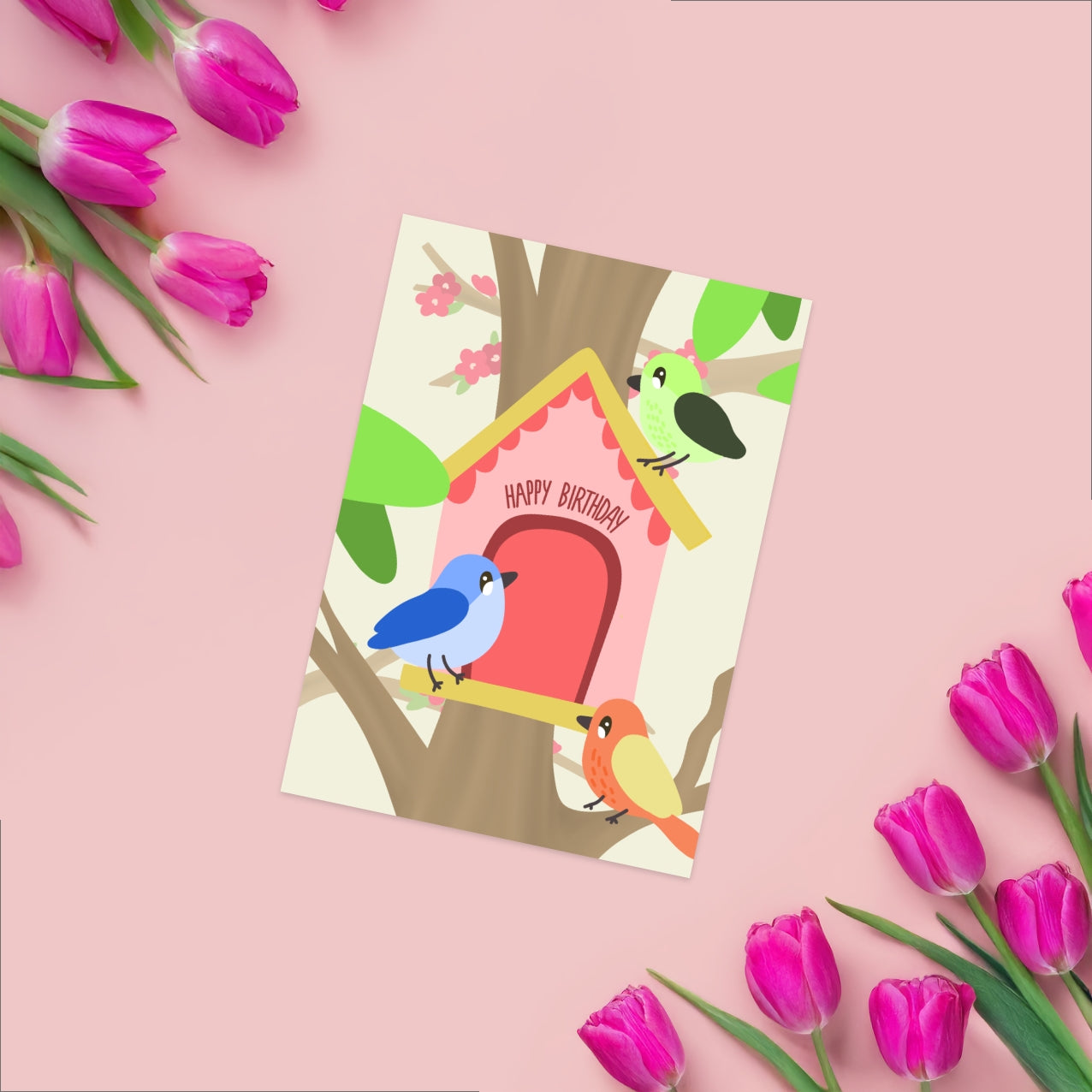 Greeting card featuring 3 colorful birds around a light pink birdhouse, the birdhouse hosts the text happy birthday above the door. 