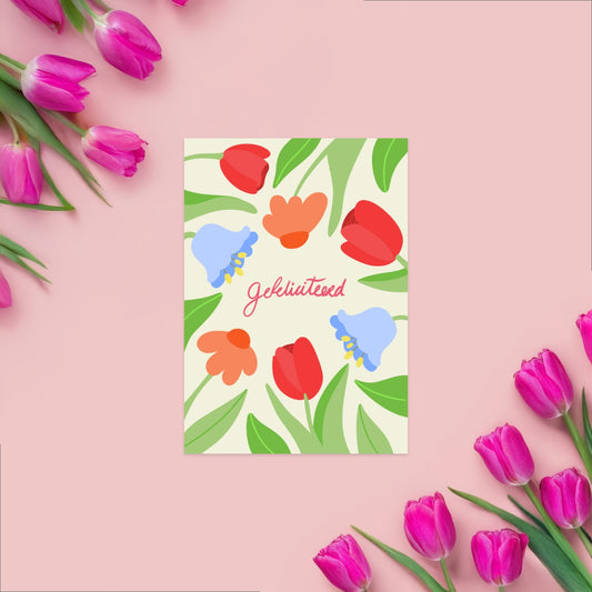 A vibrant Dutch ‘Gefeliciteerd’ card with colorful flowers emerging playfully from the side of the card. The cheerful design is set on a white background with elegant typography, perfect for any happy occasion. 