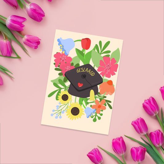 Greeting card  on a beige background with a graduation cap with geslaagd on it. around the graduation cap there are vibrant flowers and greenery. 